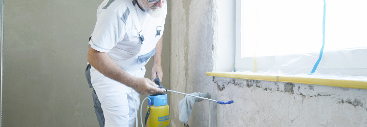 Ein Malermeister sprüht eine Wand mit Grundierung ein.